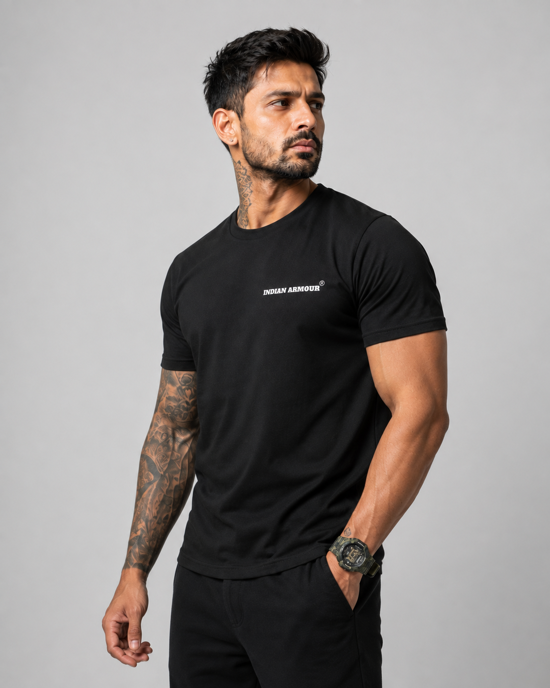 A muscular man with tattoos wearing a black short-sleeve t-shirt with a small white 'INDIAN ARMOUR' logo on the left chest, 