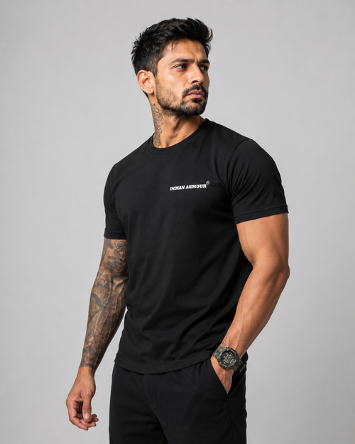 A muscular man with tattoos wearing a black short-sleeve t-shirt with a small white 'INDIAN ARMOUR' logo on the left chest, 